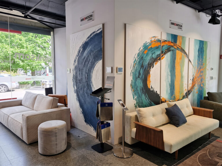 Tridelna umetniška slika triptih v teal in oranžnih tonih ob modernem raztegljivem kavču z lesenimi nasloni blagovne znamke Innovation Living v salonu Dom Ambient.