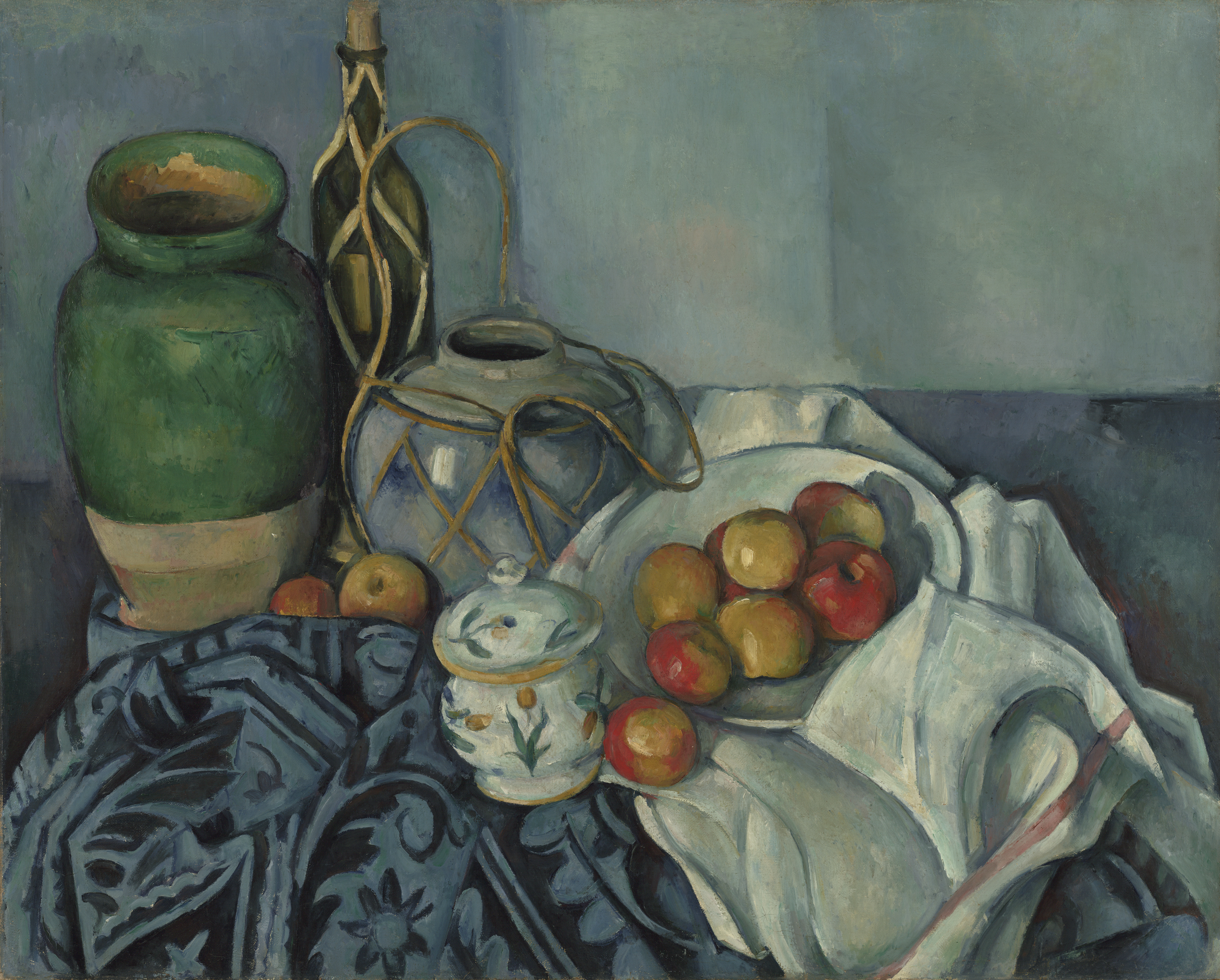 Na mizi z modro vzorčasto tkanino in belim prtom z rdečo progo stojijo zelen lonec za olive, s slamo ovita steklenica, ingverjev lonček, sladkornica in krožnik z jabolki, Paul Cézanne, 1893–1894