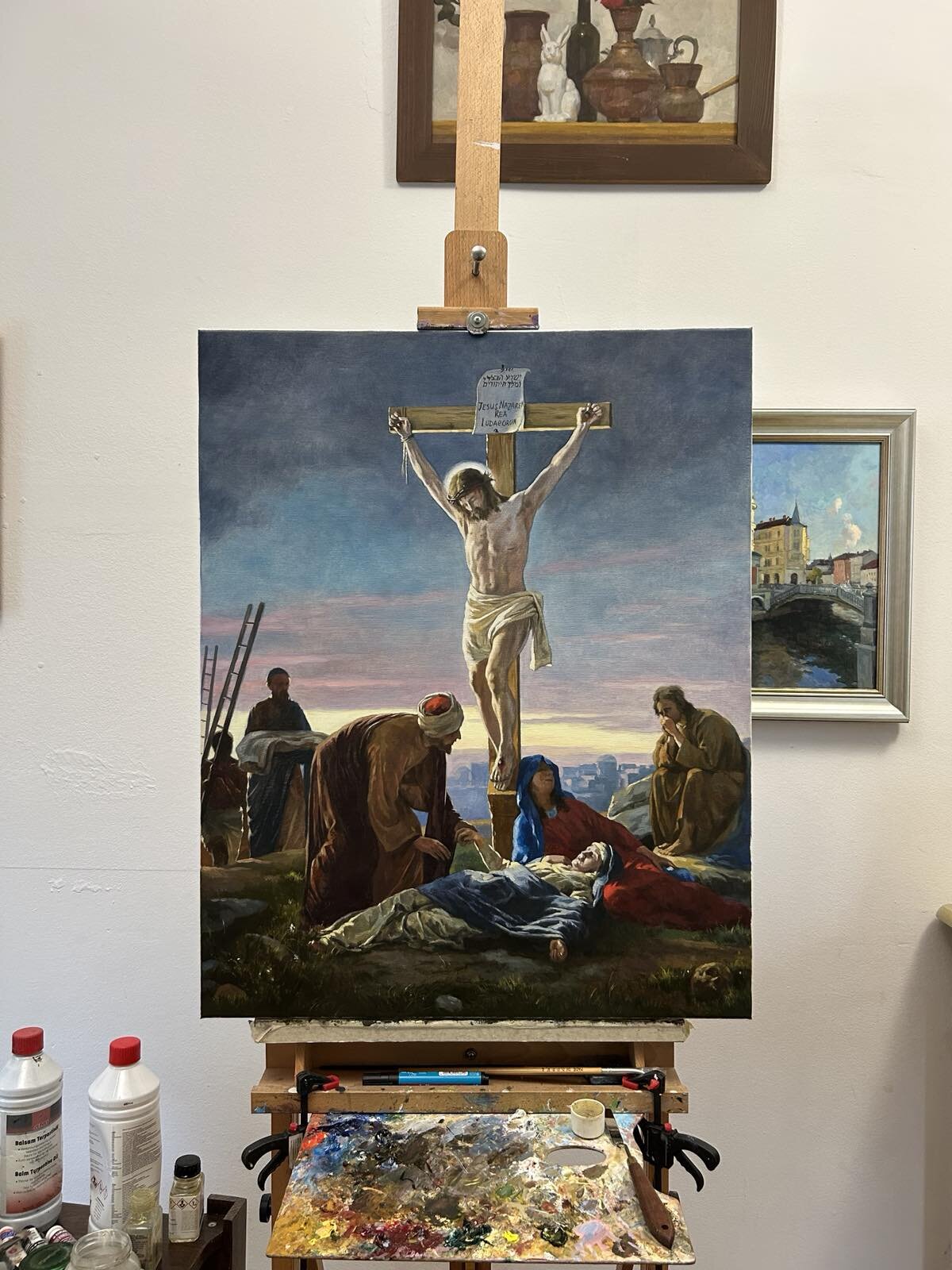 Jezus na križu – dokončana slika na platnu na stojalu, s paleto in čopiči pod njo